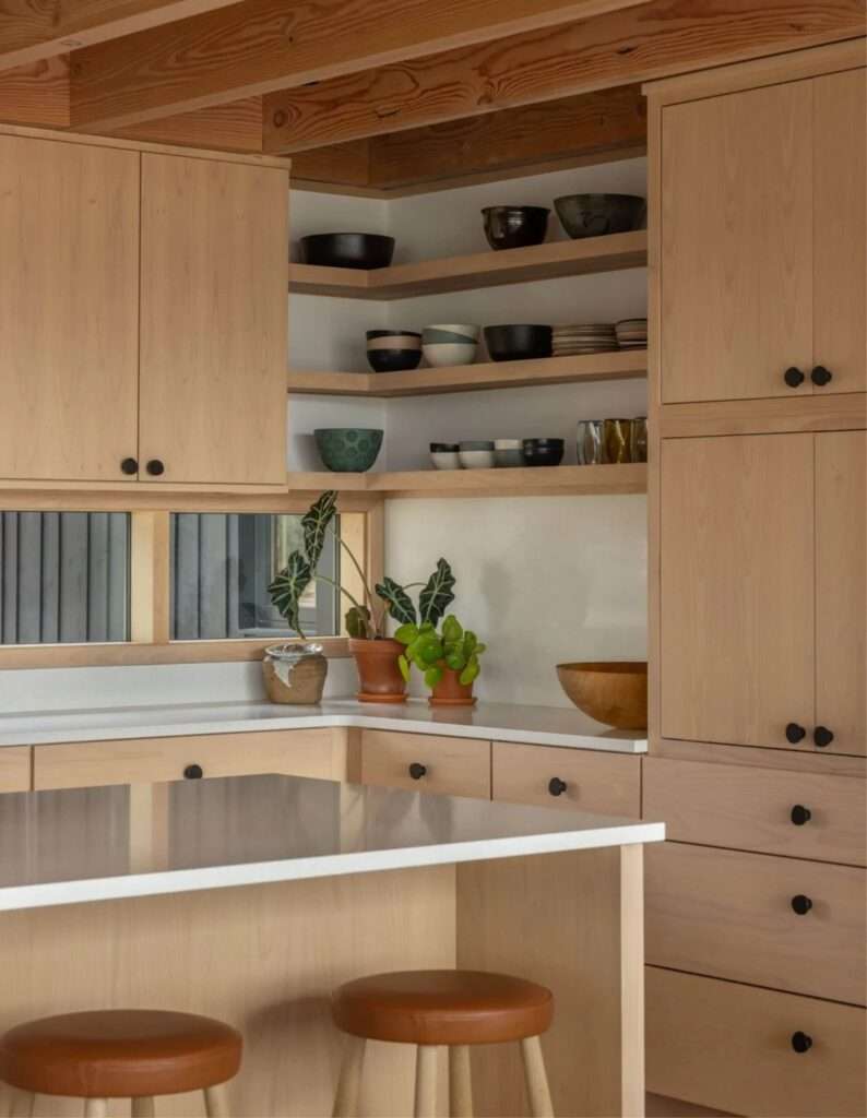 Minimalist modern kitchen with light natural wood cabinetry, white countertops, and open corner shelving.