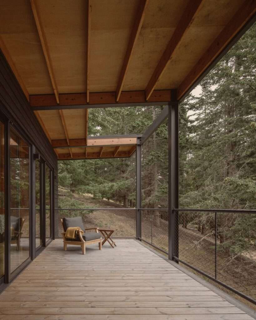 Outdoor balcony terrace of Trestle Cabin with a lounge chair and wooden table, overlooking a steep forested valley.