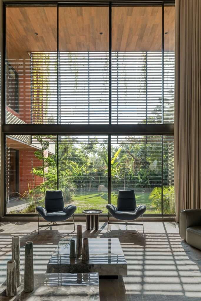 Inside-out view from a double-height living room through floor-to-ceiling glass windows looking out at a tropical garden.