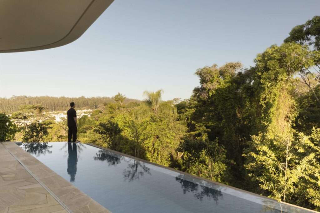 Man looking out over a sleek infinity pool integrated into the terrace of Casa Circular, overlooking a dense tropical forest valley during golden hour.