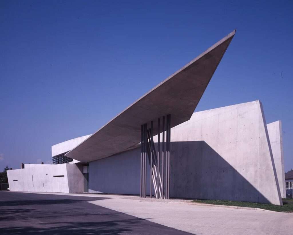 Sharp pointed concrete roof overhang extending over the driveway under a clear blue sky.