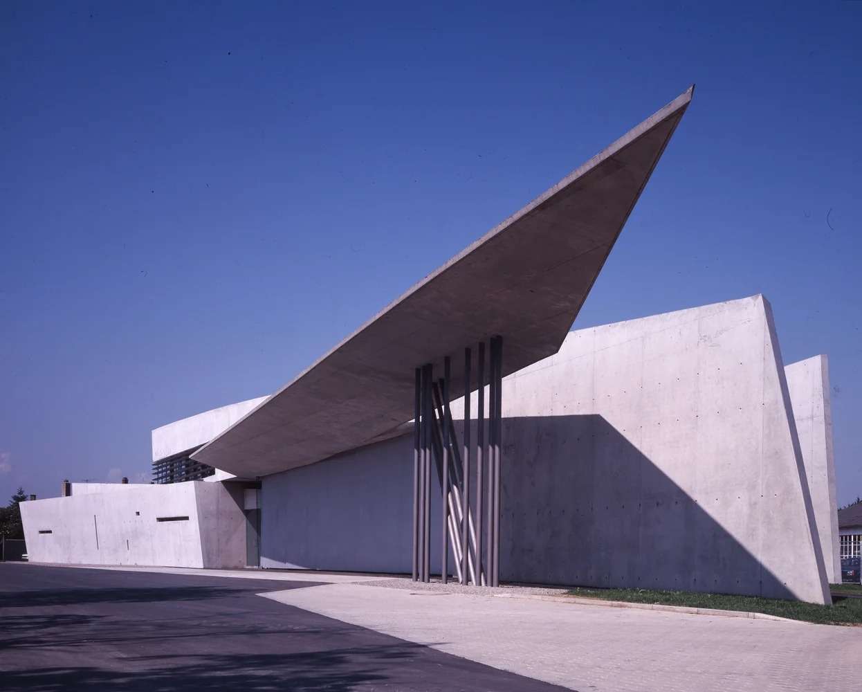 Sharp pointed concrete roof overhang extending over the driveway under a clear blue sky.