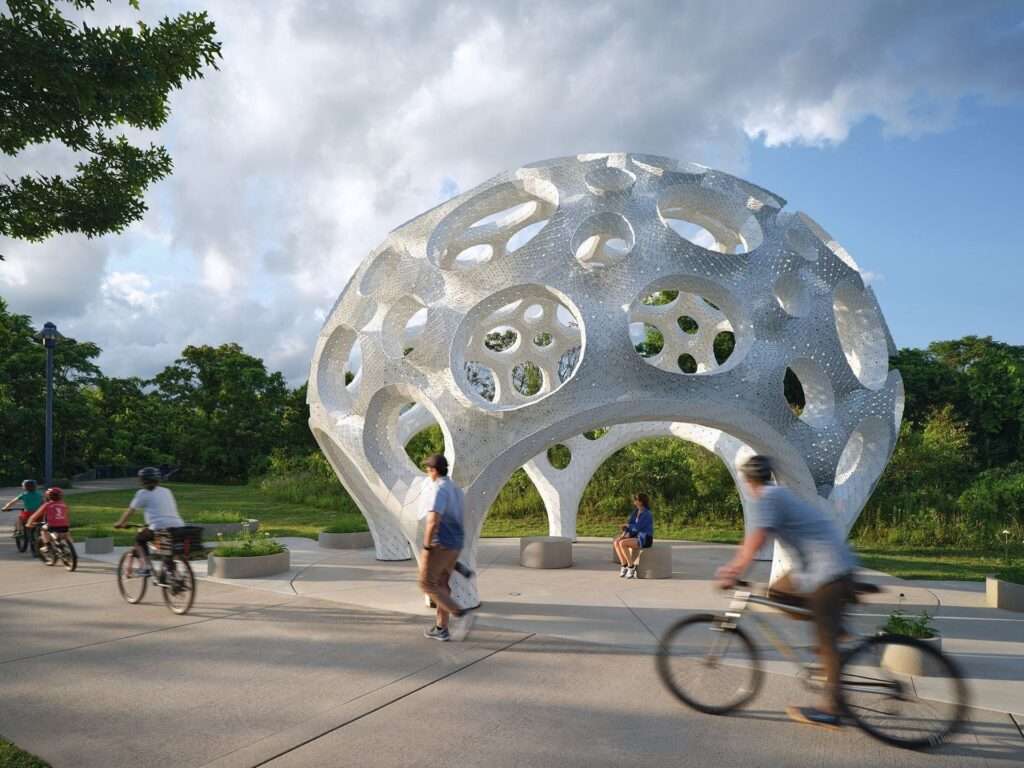 Wide shot of the Moonrise pavilion along a park path with active cyclists and pedestrians passing by under a cloudy sky.