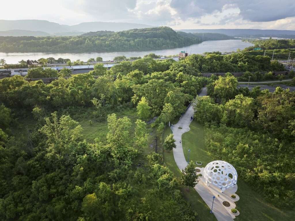 High-angle aerial drone shot of the Moonrise pavilion situated alongside a river pathway surrounded by lush green forests and hills.