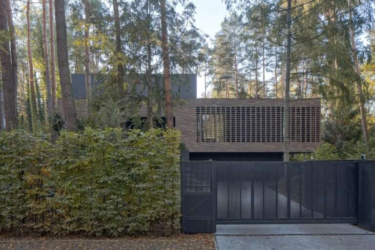 Main entrance gates and street facade of House with a Glade with a dark minimalist fence, hand-formed brick masonry screen, and towering pine tree canopy.