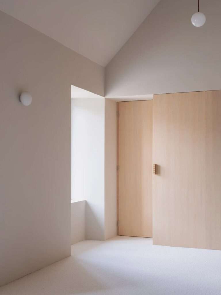 Custom integrated ash wood bookshelf and linear desk spanning a clean minimalist wall above a white modern heating radiator.