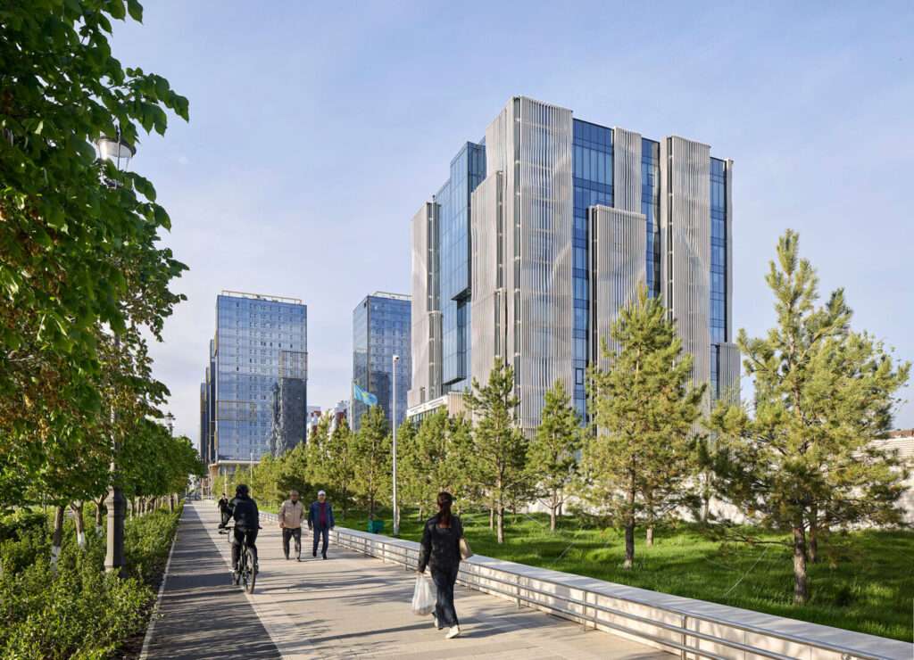 A 13-story cubic financial headquarters with stone fins seen from a landscaped pedestrian path with trees.