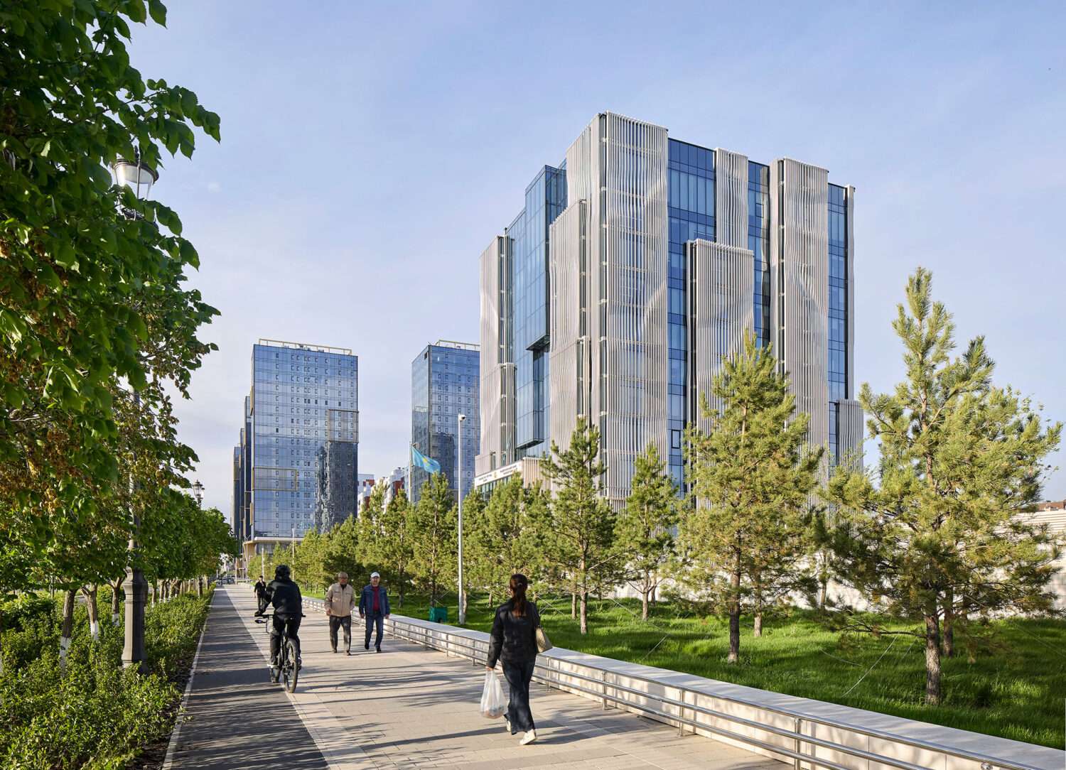 A 13-story cubic financial headquarters with stone fins seen from a landscaped pedestrian path with trees.