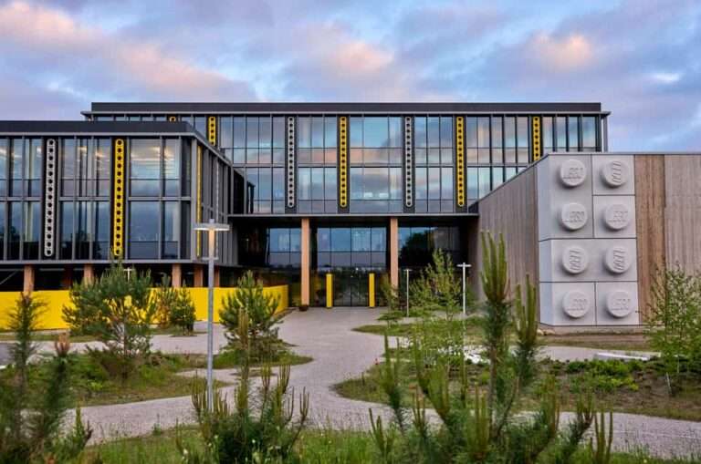A low-angle exterior view of the multi-story LEGO Kornmarken Campus building with glass fenestration and structural facade modules.