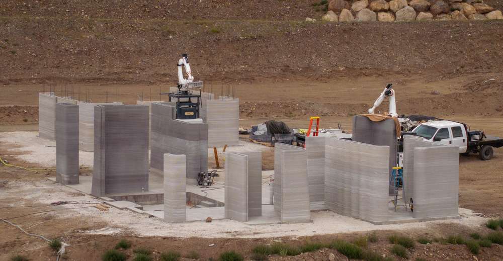 An active construction site with 3D-printed concrete walls and two robotic printing systems in Colorado.