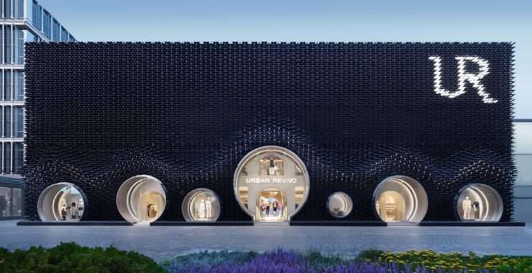 A wide nighttime shot of a dark textured facade with circular window displays and illuminated signage at the top right.