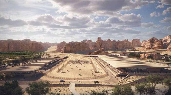 An aerial view of a desert sand arena surrounded by low-profile earth-toned buildings and rock formations.