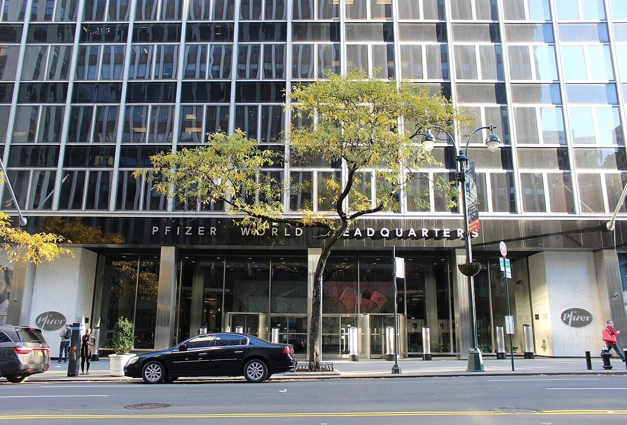 Street-level view of the glass and steel facade of the former Pfizer World Headquarters building entrance.