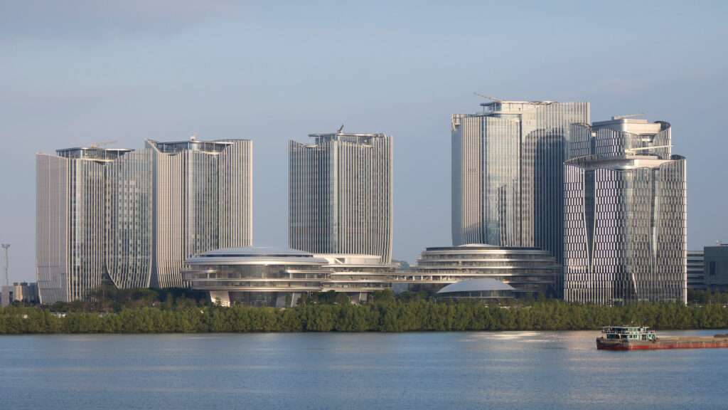 An aerial view of an architectural complex with three rounded cloud-like buildings and several skyscrapers at sunset.
