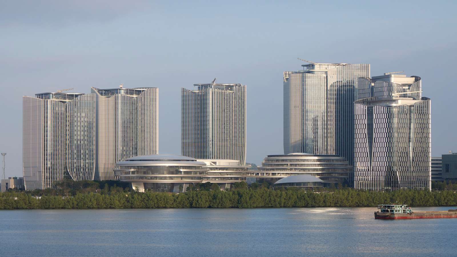 An aerial view of an architectural complex with three rounded cloud-like buildings and several skyscrapers at sunset.