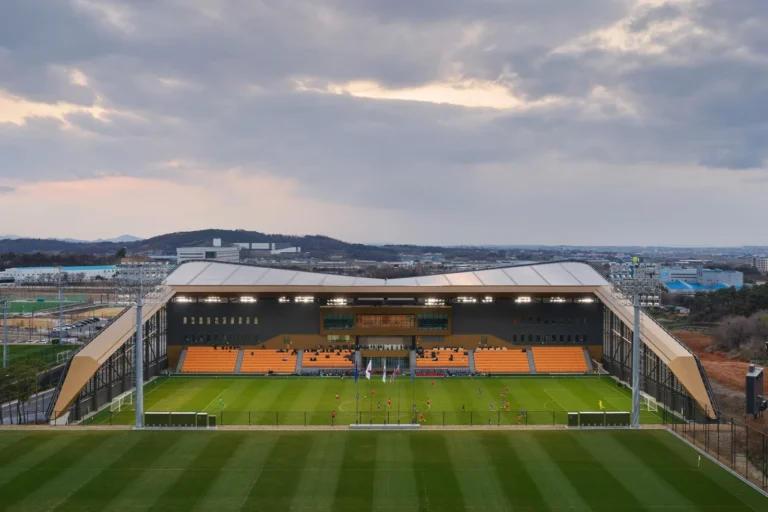 An elevated view of an outdoor football pitch and main stand with yellow seating under a cloudy sky.