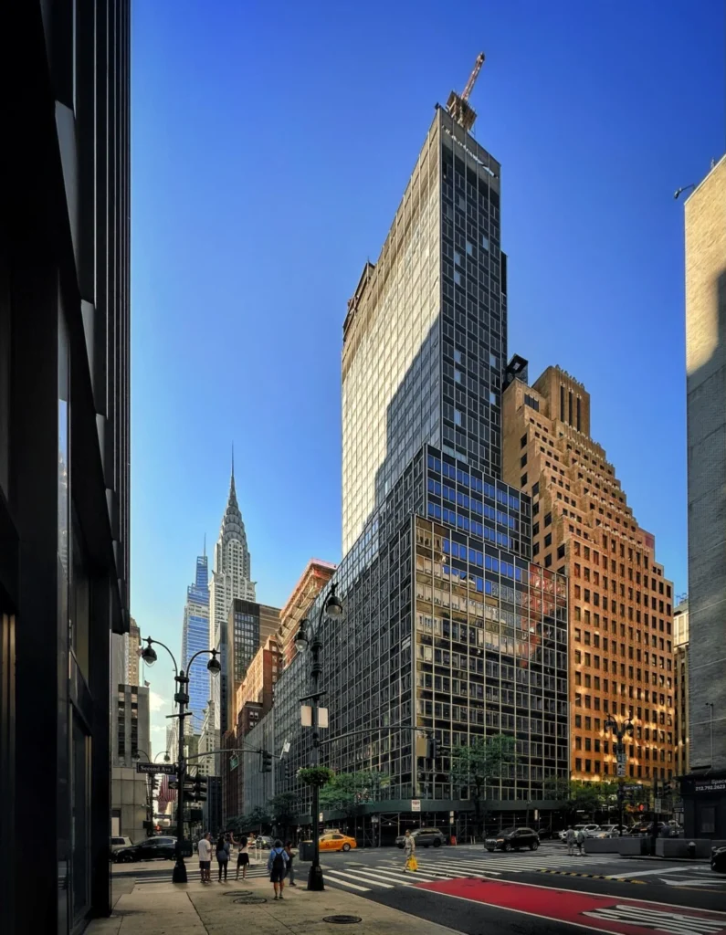 Street view looking up at a high-rise office building undergoing residential conversion with a crane on top.