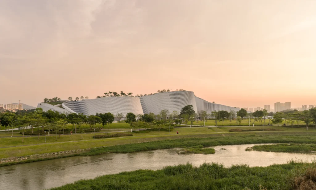 Long sweeping undulating structure clad in vertical panels across a river and parkland edge.