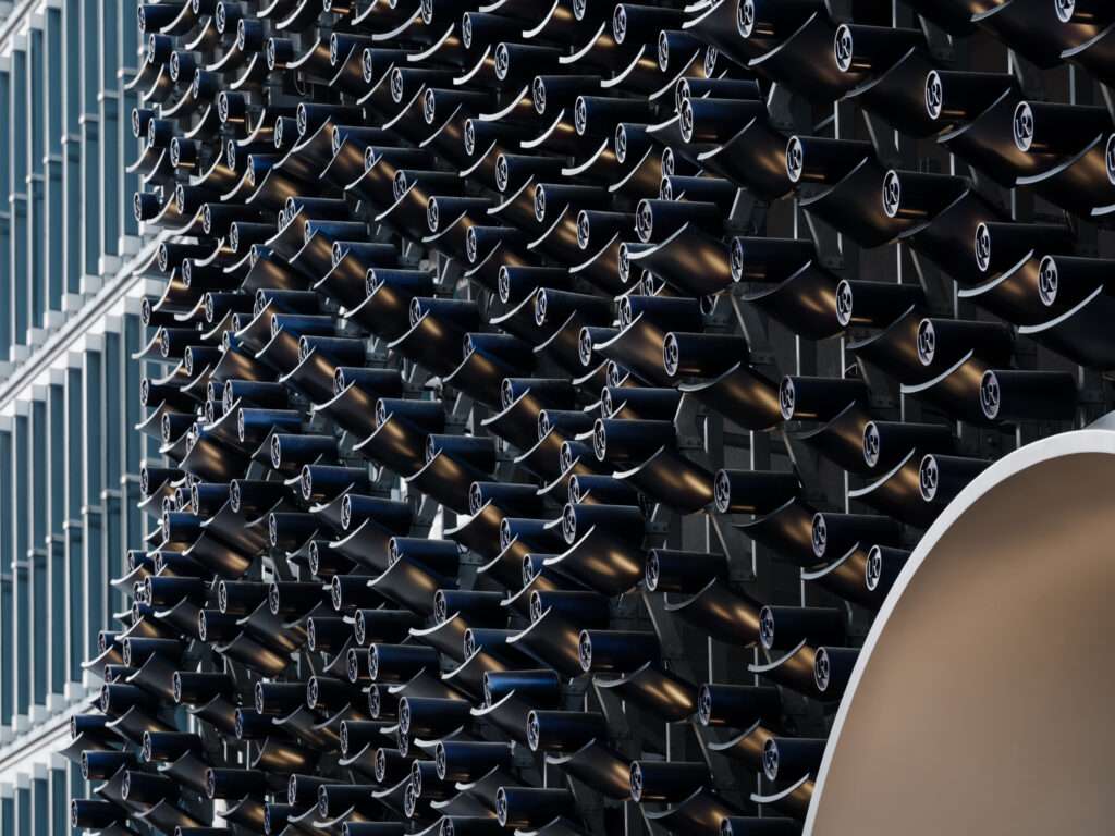 Close-up view of curved, dark aluminum tiles arranged in a repetitive pattern on a building facade.