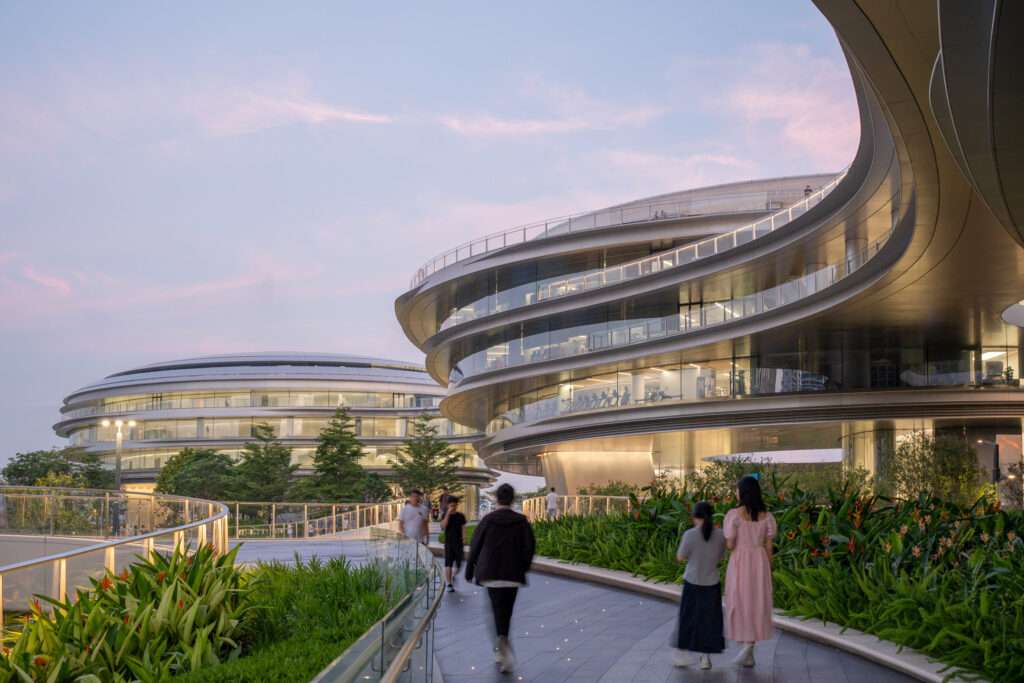 People walking on an elevated pedestrian path between the glazed curved volumes.