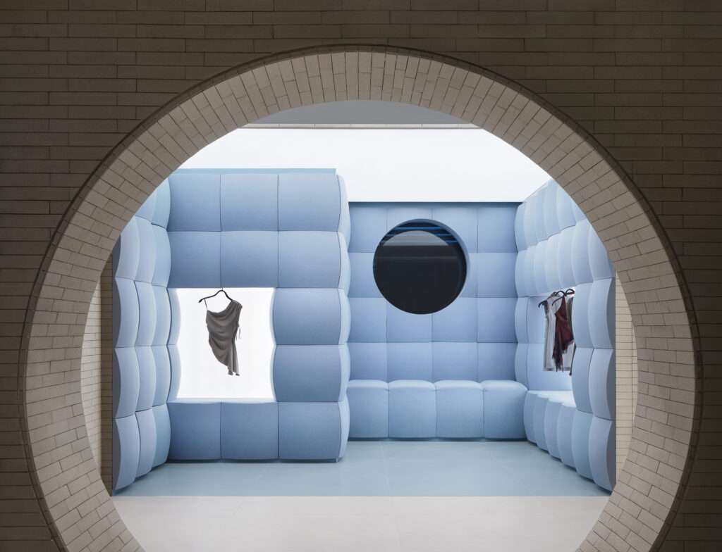 A view through a brick circular arch looking into a room with walls completely covered in light blue quilted cushions.
