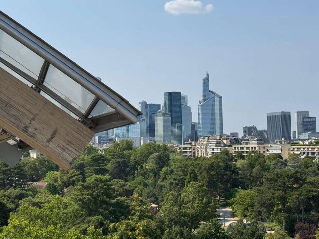 A scenic view from an elevated building terrace looking out over a dense green forest toward the modern skyline of La Défense skyscrapers in Paris.