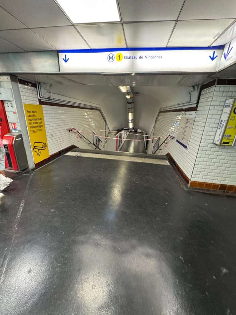A descending staircase into a Paris Metro station for Line 1 taped off and closed to the public with red and white barrier tape.