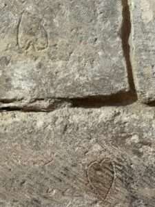 Close-up of rough, textured stone blocks forming an ancient wall, featuring faintly carved heart-like shapes or mason's marks on the surface.