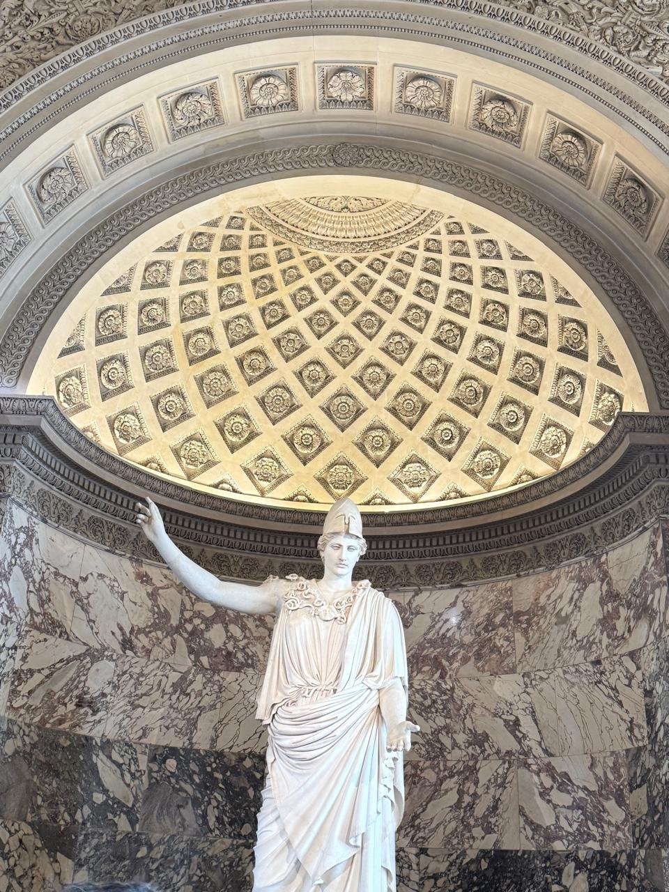 Athena, known as the Pallas of Velletri, displayed beneath a coffered half dome and framed by veined marble walls at the Louvre.