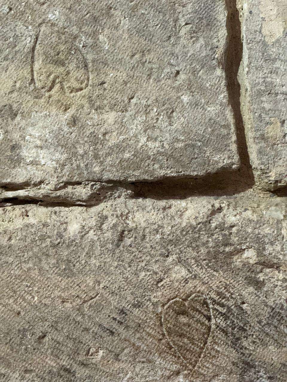 Close-up of rough, textured stone blocks forming an ancient wall, featuring faintly carved heart-like shapes or mason's marks on the surface.