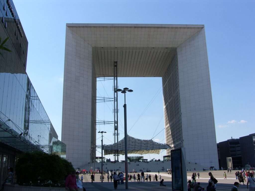 The monumental Grande Arche de la Défense towering over the concrete plaza, with its massive white marble facade and tensioned canopy structure visible in the center.