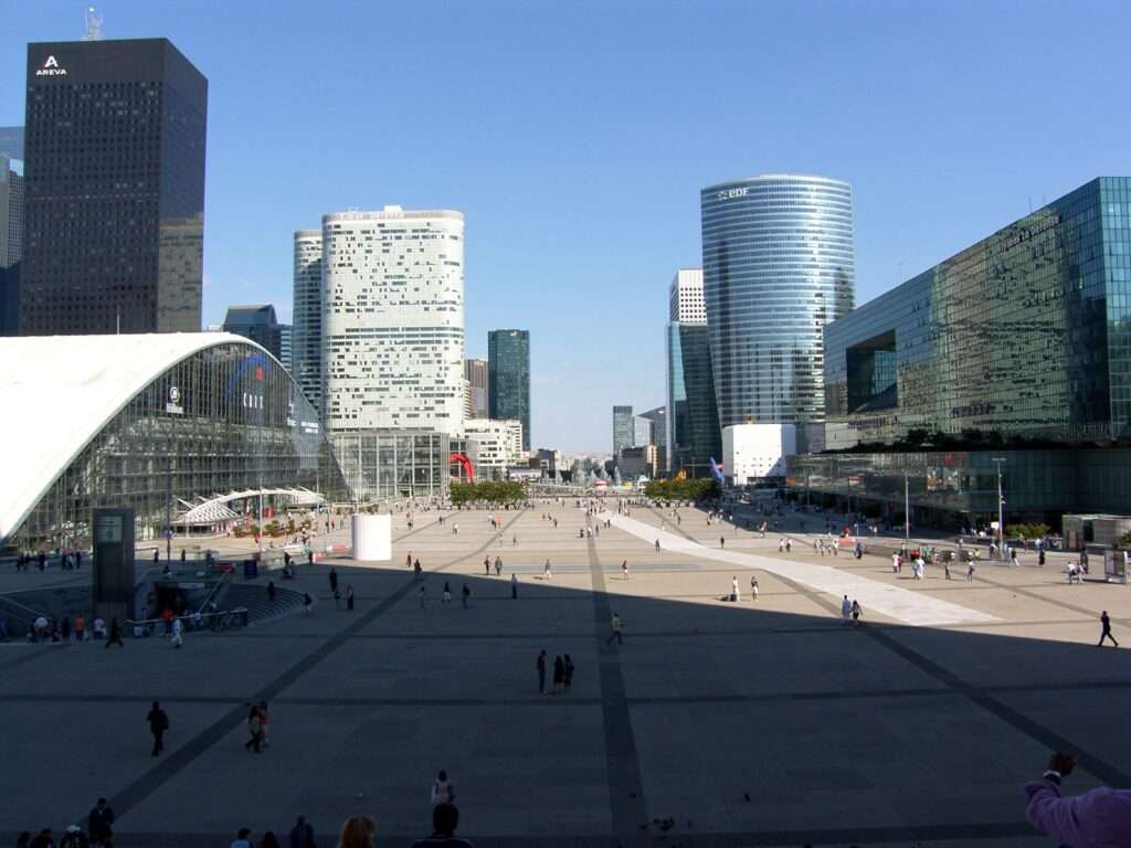 Wide view of La Défense in 2006, featuring the CNIT building, Areva tower, and EDF tower surrounding a vast, sparsely populated concrete pedestrian esplanade.
