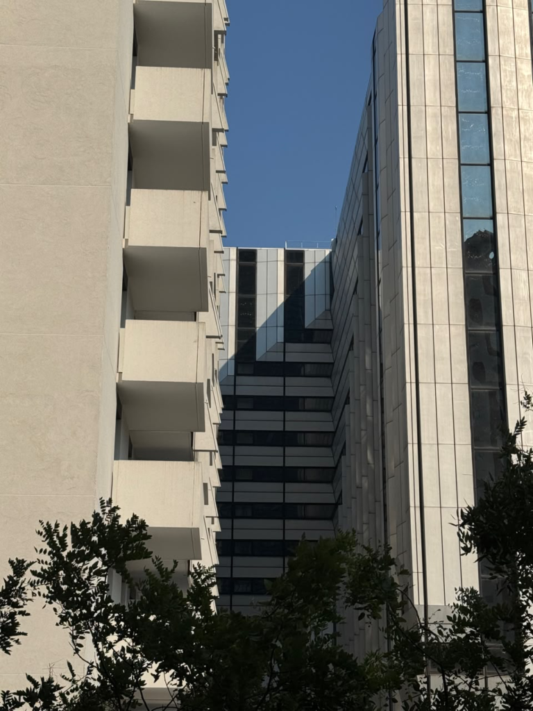 Low-angle view looking up between a textured concrete residential building with protruding balconies and a modern skyscraper with vertical glass panels against a blue sky in La Défense.