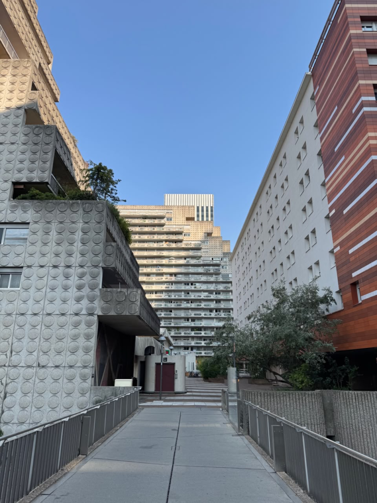 Concrete walkway leading towards tiered brutalist apartment buildings under a clear blue sky