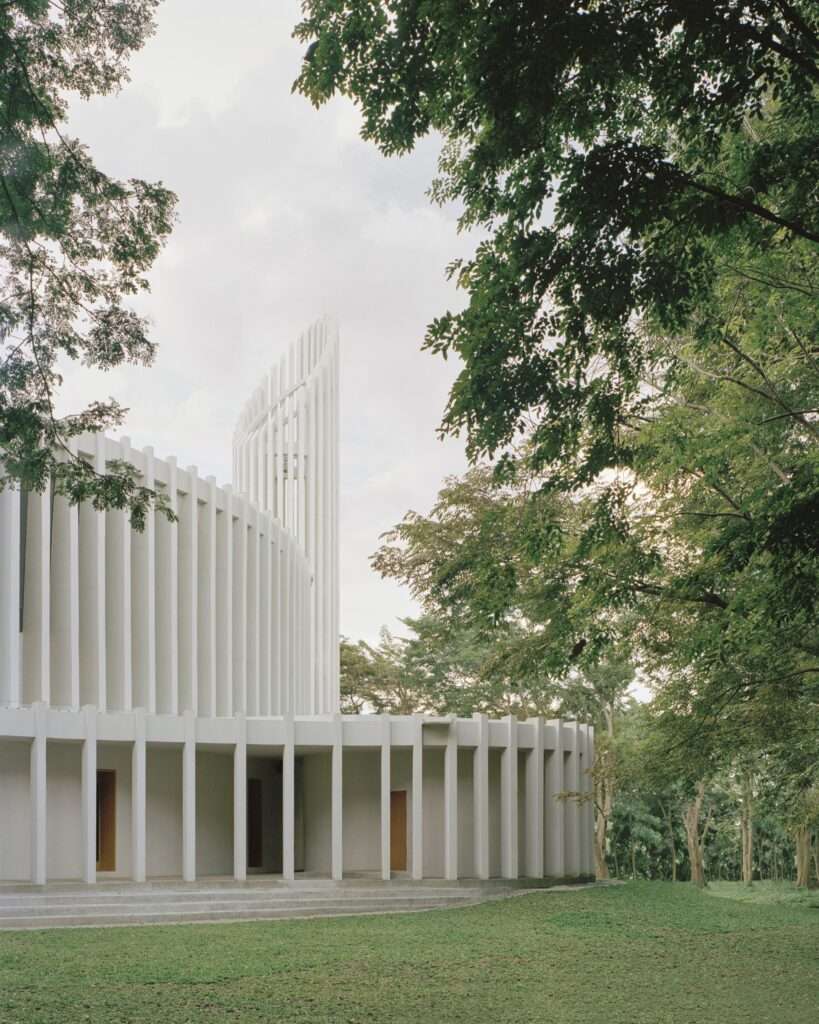 Side view of Santuario de La Salle showing the soaring vertical bell tower structure composed of parametric white fins adjacent to lush trees.