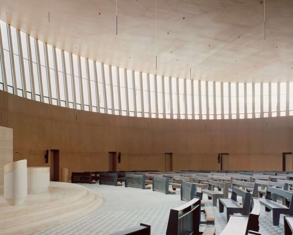 Interior of Santuario de La Salle showing curved warm wood walls, clerestory windows, and arranged wooden pews facing the sanctuary altar.