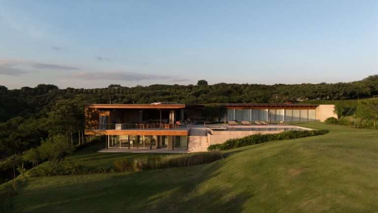 Aerial view of Casa Flow featuring a sloped lawn, wooden roof structure, outdoor swimming pool, and two-level layout integrated into the surrounding landscape.