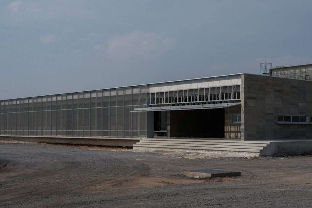 Wide exterior view of the elongated single-story building at the LPP Rice Grading Center, featuring a concrete stepped entry and a full-length mesh sunscreen.