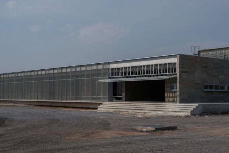 Wide exterior view of the elongated single-story building at the LPP Rice Grading Center, featuring a concrete stepped entry and a full-length mesh sunscreen.