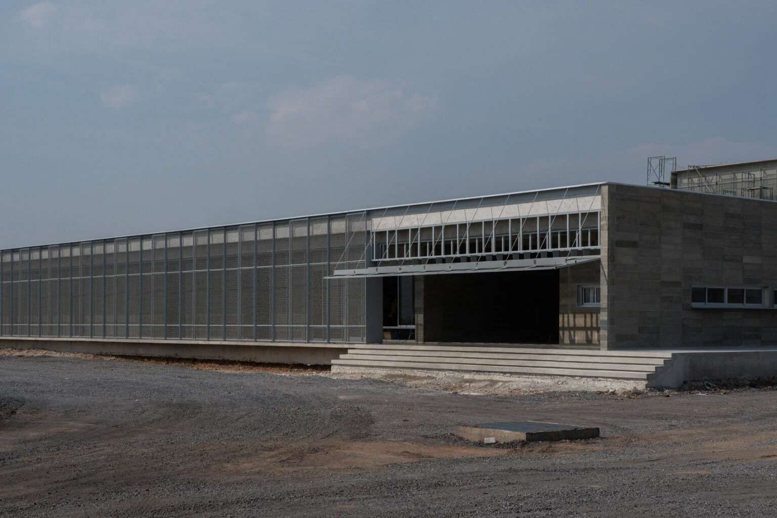 Wide exterior view of the elongated single-story building at the LPP Rice Grading Center, featuring a concrete stepped entry and a full-length mesh sunscreen.