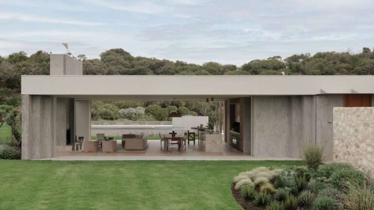 Open-plan glass pavilion of Wildcoast House showing living and dining areas connected directly to the outdoor lawn and landscape.
