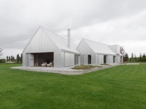Modern lake house exterior showing corrugated aluminum panels and folding doors opening to a warm wooden interior terrace.