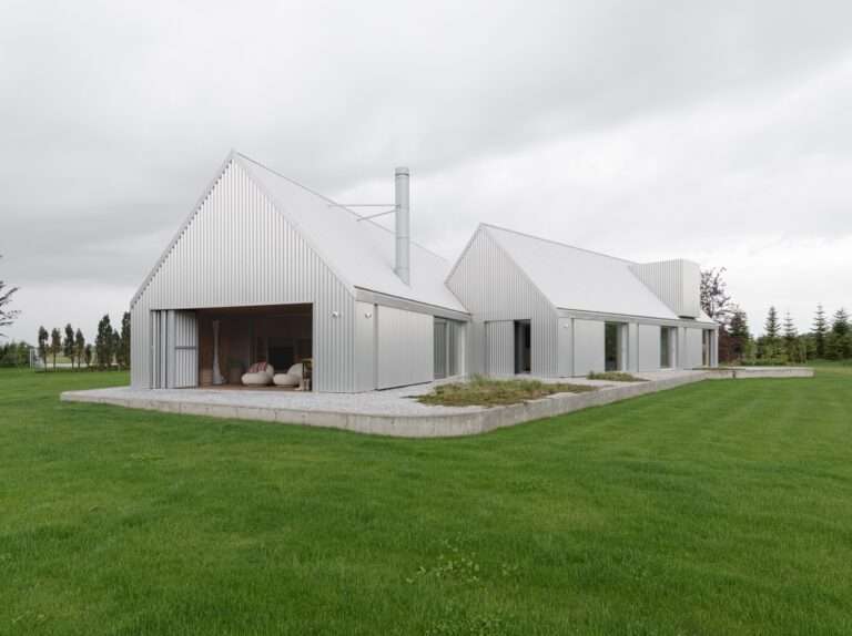 Modern lake house exterior showing corrugated aluminum panels and folding doors opening to a warm wooden interior terrace.