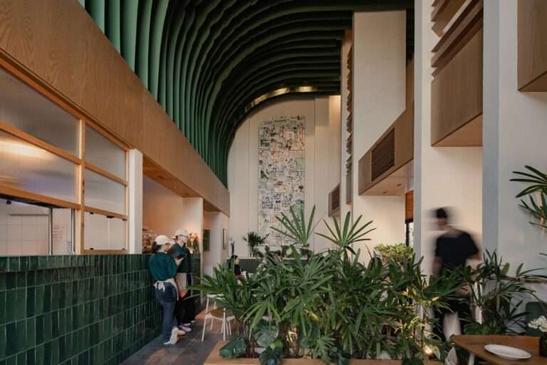 High-angle view of Mimado Restaurant interior showing double-height space, green fabric ceiling installation, recycled book artwork mural, and green tiled counter with indoor plants.