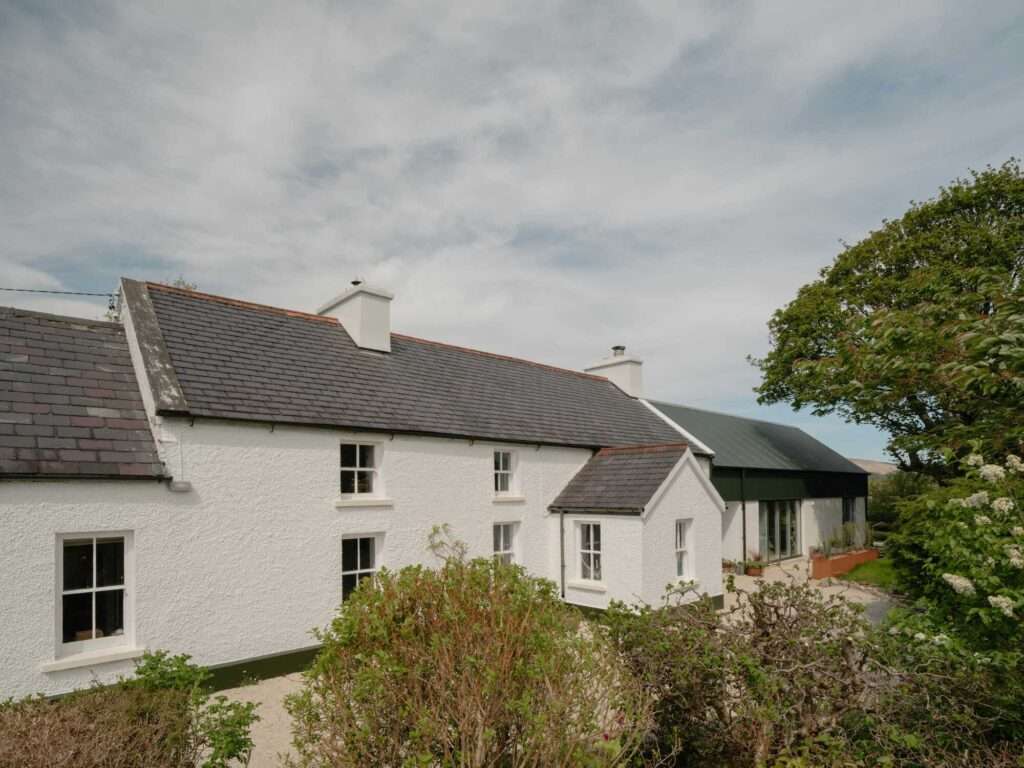 Exterior view of Kettle's Yard Farm showing a historic white cottage with a slate roof connected to a modern dark green extension.
