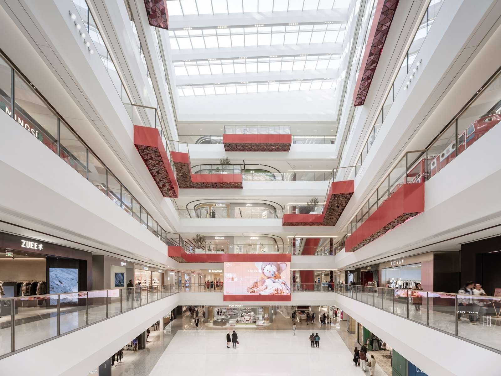 Main central atrium of Wuxi MixC Mall featuring multi-level white terraces, sculptural red walkways, a massive LED screen, and a large glass skylight illuminating the open retail environment.