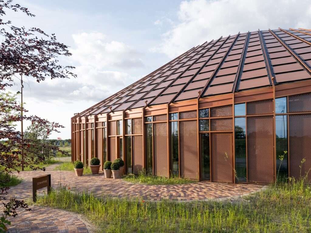Close-up of the textured wooden facade and sloping roof of Dymak HQ with potted plants and brick pathway.