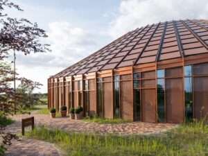Close-up of the textured wooden facade and sloping roof of Dymak HQ with potted plants and brick pathway.