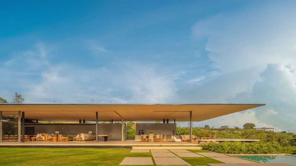 Wide exterior view of JF Residence showing a minimalist single-story pavilion with an expansive flat roof, open-plan living area, and integrated infinity pool amidst a rural landscape.