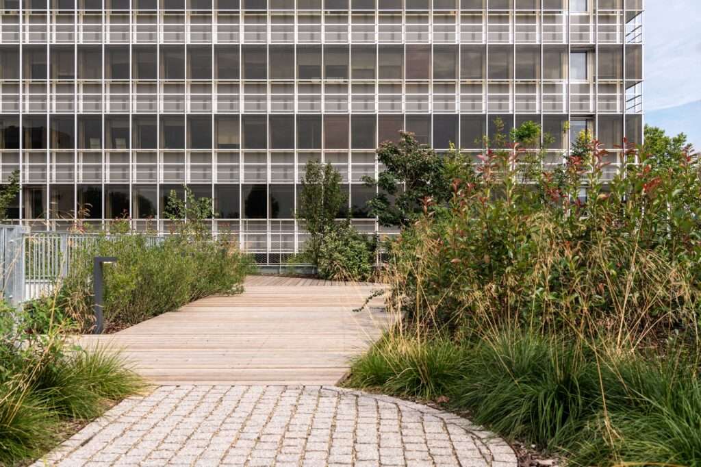 Rooftop view of a lush vertical garden with a wooden pedestrian walkway in The Silo, overlooking an existing building facade.